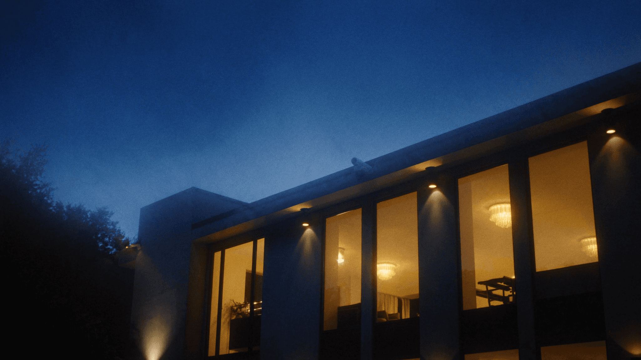 A Connecticut home at blue hour with warm window light and a security camera on the eave